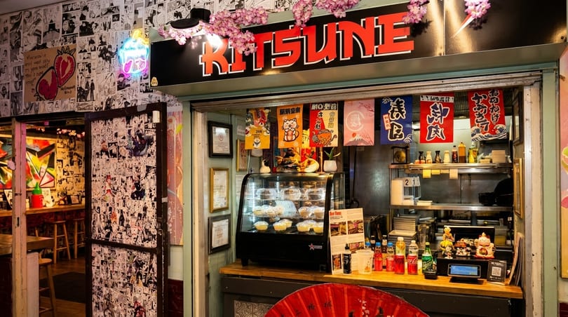 The Kitsune restaurant entrance, featuring a vibrant manga-covered wall and a food display.