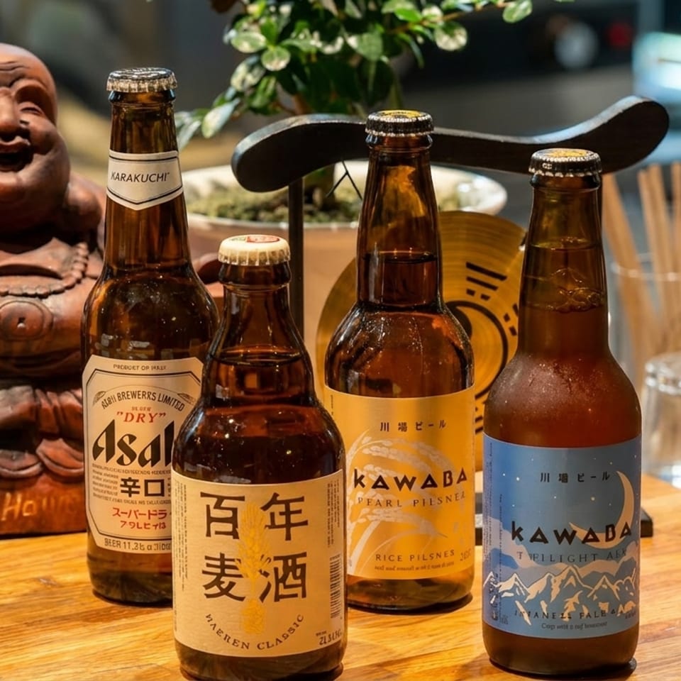 Four bottles of Japanese beer, including Asahi and Kawaba, on a wooden table next to a Buddha statue.